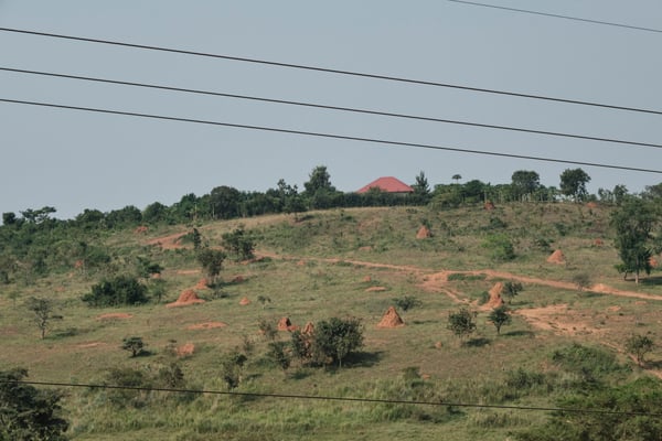 Hillside view with several large ant hills and a building that resembles the sun coming up over the horizon, Entebbe, Uganda