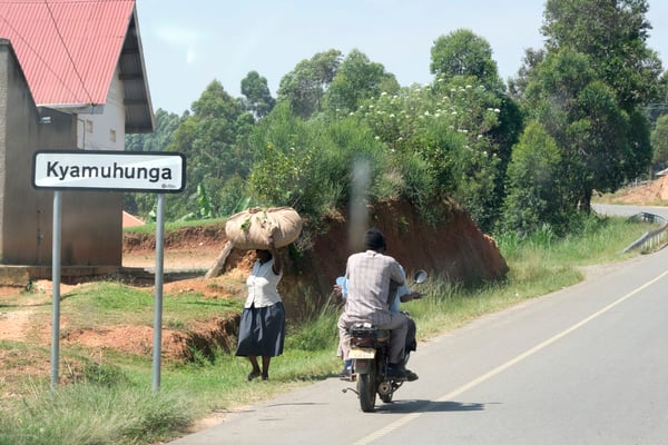 Kyamuhunga town sign, person on a motorcycle and person carrying a bundle on their head, Uganda