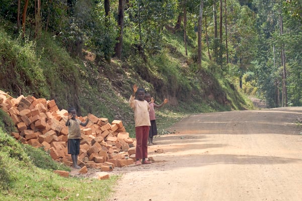 Three kids waving with their hands covered in brick dust, Uganda